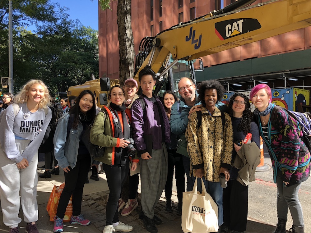 Ten People pose together outside with a construction site behind them